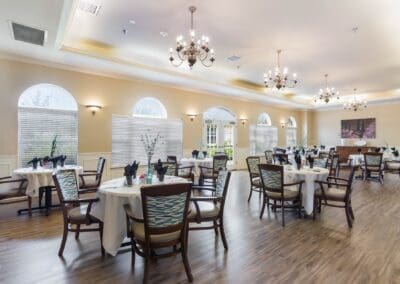 Large dining space with table and chair sets, centerpieces, windows, chandeliers, and hardwood floors